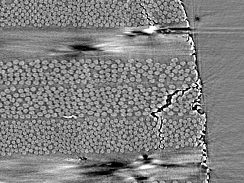 A real synchrotron CT slice of a carbon-fibre laminate near its free edge, with cracks in three ply orientations outlined in white.